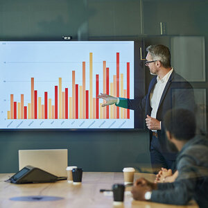 A man in front of a bar graph giving a presentation. A man in front of a bar graph giving a presentation.