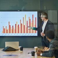 A man in front of a bar graph giving a presentation. A man in front of a bar graph giving a presentation.