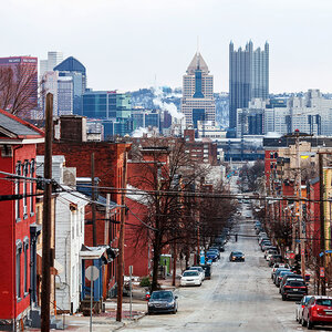 A street view of a working-class neighborhood with the skyline of a wealthy business district in the background – Pittsburgh.