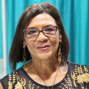 A woman with shoulder length brown hair wearing glasses poses for the camera at a press event – a photo of Sonia Manzano. A woman with shoulder length brown hair wearing glasses poses for the camera at a press event – a photo of Sonia Manzano.