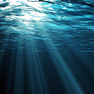 An underwater photo of light streaming into dark blue water.