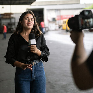A young female reporter in a factory speaks into a microphone. A young female reporter in a factory speaks into a microphone.