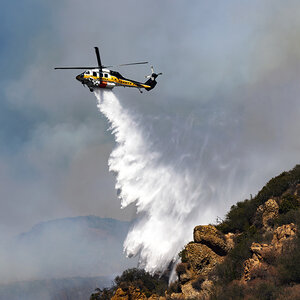 A helicopter sprays water over wildfire areas. A helicopter sprays water over wildfire areas.