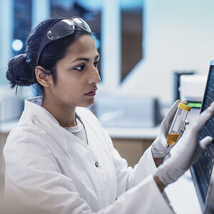 A medical researcher of South Asian descent inputs data to a computer screen.