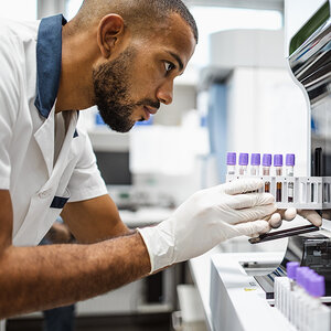 A scientist wearing gloves inserts lab vials into a machine. A scientist wearing gloves inserts lab vials into a machine.