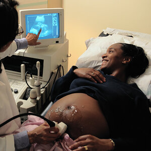 A pregnant African American woman smiles as she views a computer screen during an ultrasound.