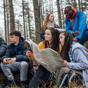A group of teenagers with their teachers in the woods using maps. A group of teenagers with their teachers in the woods using maps.