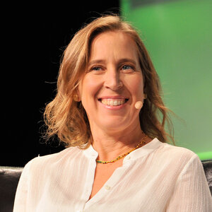 A seated woman with shoulder-length blond hair wearing a linen blouse looks to her right – a photo of Susan Wojcicki.