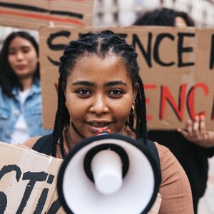 Young woman of color holding a megaphone and protest sign with other protestors of color behind her holding signs. Young woman of color holding a megaphone and protest sign with other protestors of color behind her holding signs.