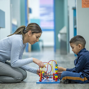 A child and therapist sit on the floor playing. A child and therapist sit on the floor playing.