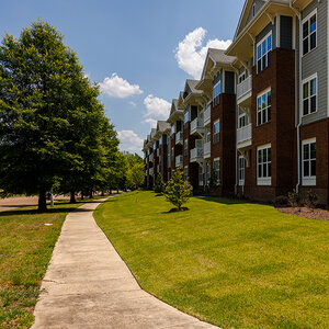 A row of low-rise brick apartment buildings surrounded by grass trees.