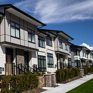 A row of two-story attached homes under a blue sky with clouds. A row of two-story attached homes under a blue sky with clouds.
