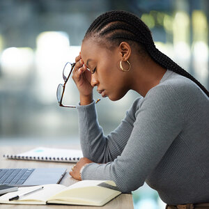 A tired office worker removes her glasses and closes her eyes while seated at her desk. A tired office worker removes her glasses and closes her eyes while seated at her desk.