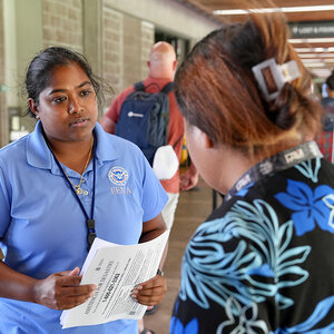 A relief worker in a light blue shirt distributes information to a disaster victrim.