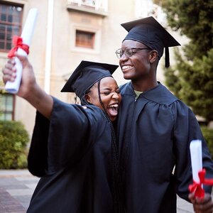 Two college graduates hugging with their diplomas in hand.