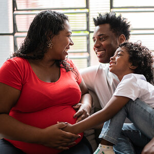 A pregnant African American woman sits with her husband and son.