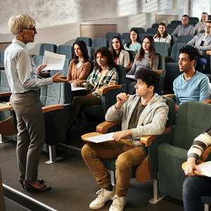A female college professor lectures to a room of students. A female college professor lectures to a room of students.