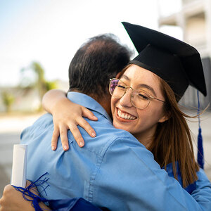 A graduate hugging a family members with a diploma in her hands. A graduate hugging a family members with a diploma in her hands.