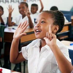 A young African girl raises her hands during math class. A young African girl raises her hands during math class.