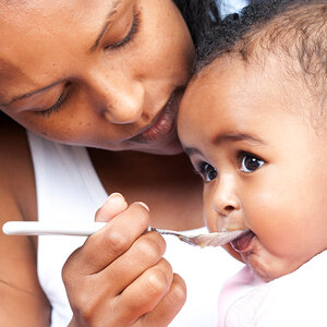 A mother feeds her infant with a spoon.