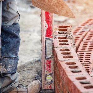 A bricklayer holds a level against a curved wall being built. A bricklayer holds a level against a curved wall being built.