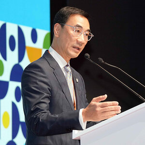 A Chinese man in a business suit and wearing glasses speaks into a microphone – a photo of Michael Lee. A Chinese man in a business suit and wearing glasses speaks into a microphone – a photo of Michael Lee.