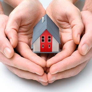 A child’s hands nested in an adult’s hands holding a small model of a house.