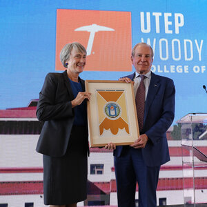 A woman and man stand on a stage holding a plaque.