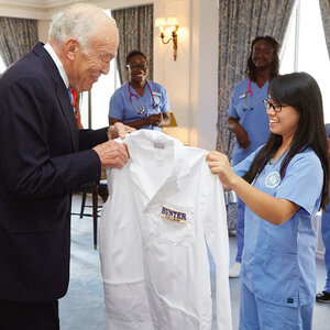 Leonard Lauder handing a white coat to a Hunter College student.