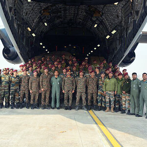 A rescue team poses for picture at the open back of a large military transport aircraft.
