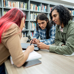 Three students studying in a library. Three students studying in a library.
