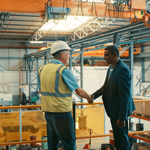 A manufacturing worker and executive shake hands in a warehouse.