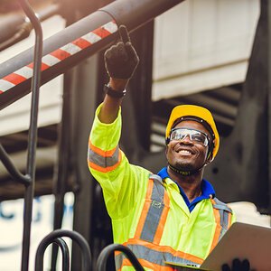 Worker of color in safety glasses and helmet pointing.