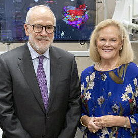 A well-dressed older couple pose for a photo in front of medical equipment—an image of John and Sarah Lechleiter. A well-dressed older couple pose for a photo in front of medical equipment—an image of John and Sarah Lechleiter.