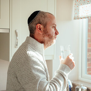 A Jewish man stand in front of his kitchen window.
