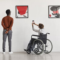 Two people, one standing and one in a wheelchair, in a museum. Two people, one standing and one in a wheelchair, in a museum.