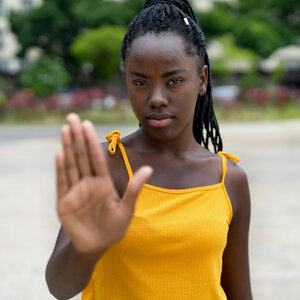 A young African-American woman in a yellow shirt gestures with her hand to stop.