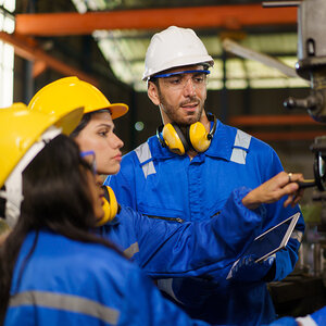 A factory supervisor trains two female employees to operate a machine.