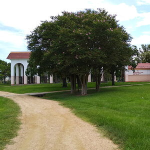 A Spanish style park pavilion foregrounded by a tree and gravel path.