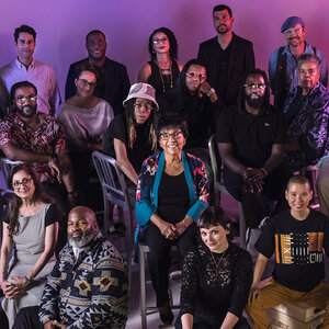 Several artists - some seated, some standing - pose for a group photo. Several artists - some seated, some standing - pose for a group photo.