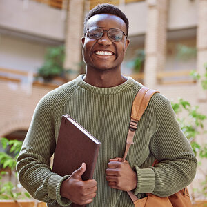 A college student holding his notebook and backpack smiles at the camera. A college student holding his notebook and backpack smiles at the camera.