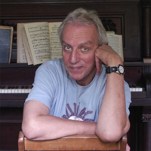 A man poses for a photo with a piano in the background – a photo of John Aielli. A man poses for a photo with a piano in the background – a photo of John Aielli.