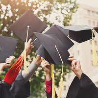 A group of unidentifiable graduates preparing to toss their mortarboards in the air.