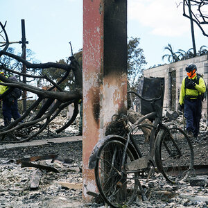 A bicycle, badly damaged by fire leans agaisnst the remains of a burned out building.