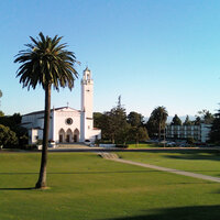 A Spanish style chapel painted white sits in a garden with a palm tree in the foreground. A Spanish style chapel painted white sits in a garden with a palm tree in the foreground.