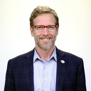 A man with sandy hair, beard, and glasses, wearing a suit jacket smiling at the camera – a photo of Joel Clement.