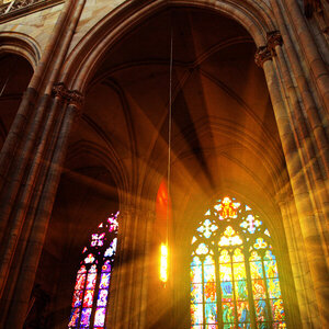 The interior of a gothic church as light shines through multicolored stained-glass windows.