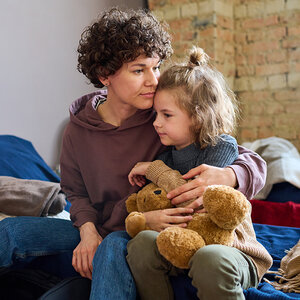 A woman and her child sit on a bed in a women’s shelter.