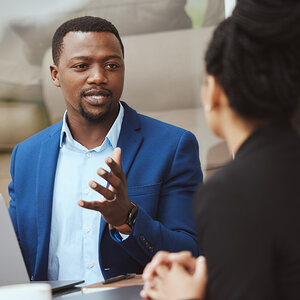 An African American businessman in conversation with a woman gestures with his hand.