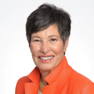 A woman with short hair in an orange suit jacket - a photo of Lyda Hill.
